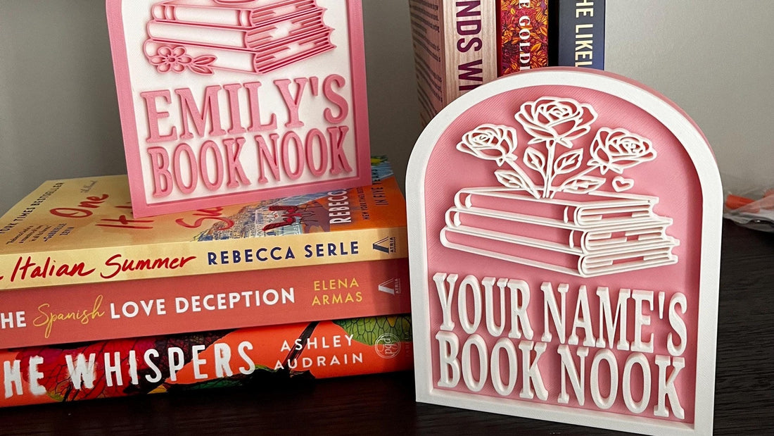 Two pink personalized book nook signs, one reading Emily's Book Nook, on books