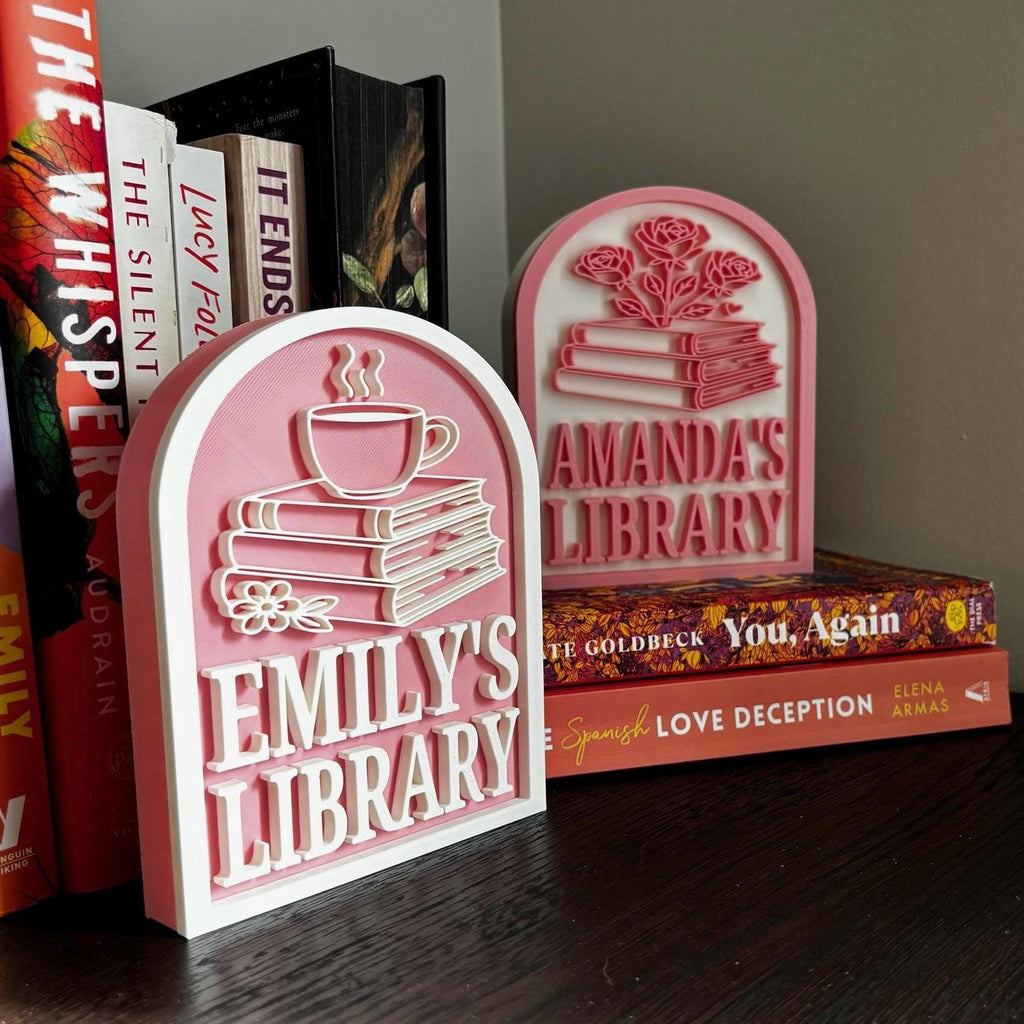Personalized pink bookshelf signs with book and cup designs, displayed with novels for book lovers