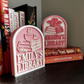 Personalized pink bookshelf signs with book and cup designs, displayed with novels for book lovers