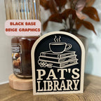 Personalized library sign with beige text and graphics on black base, books and coffee cup design