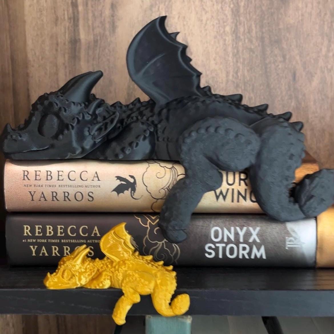 Sleeping black 3D‑printed PLA dragon curled atop hardcover books on a wood shelf, Empyrean Series fantasy decor – perfect gift for book lovers and fans of Fourth Wing-inspired home accents