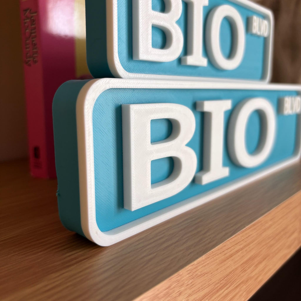 Close angled view of the raised white lettering on the teal BIO BLVD street signs