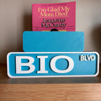 Back of the small teal sign behind the large BIO BLVD street sign
