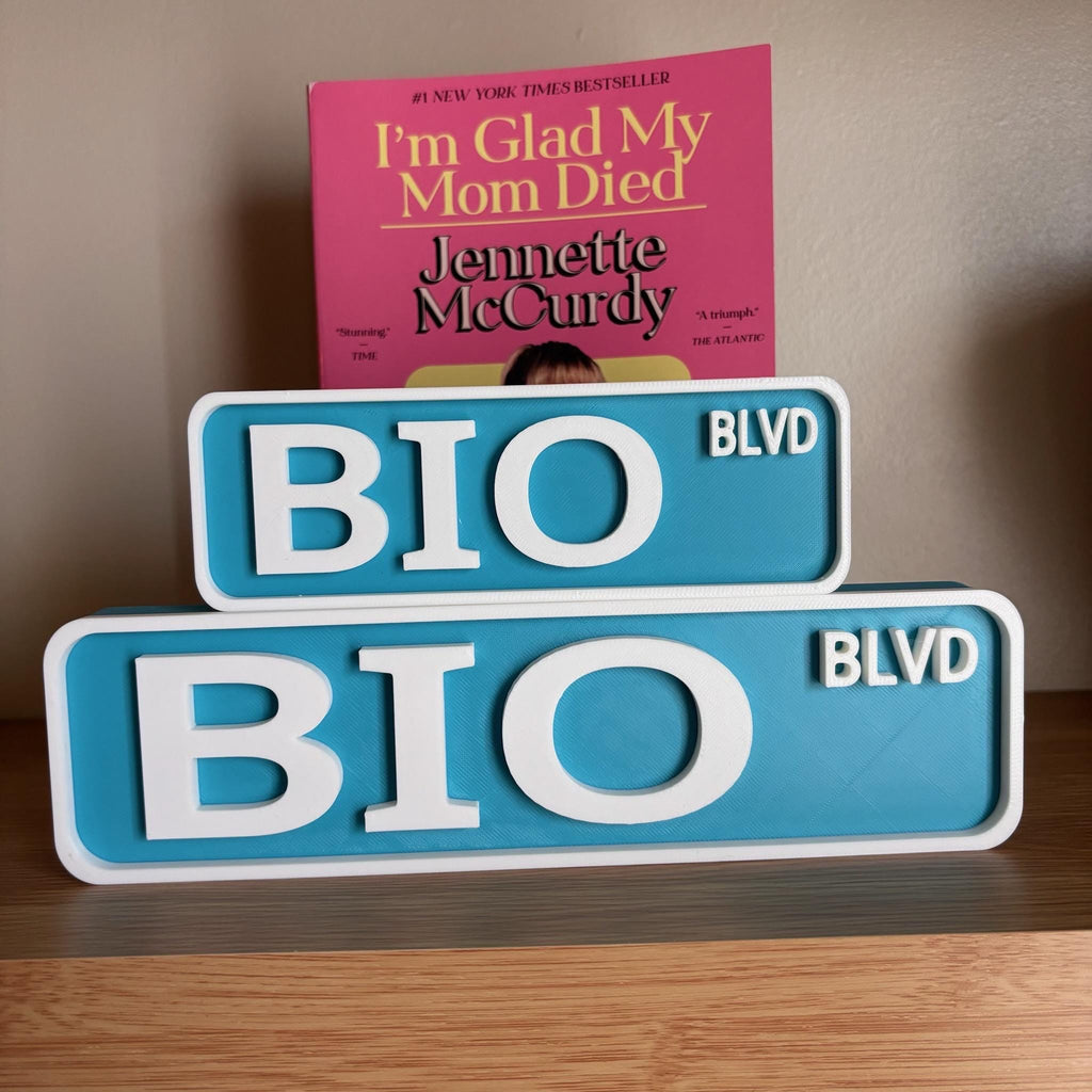 Small and large teal and white BIO BLVD street signs stacked on a wooden shelf