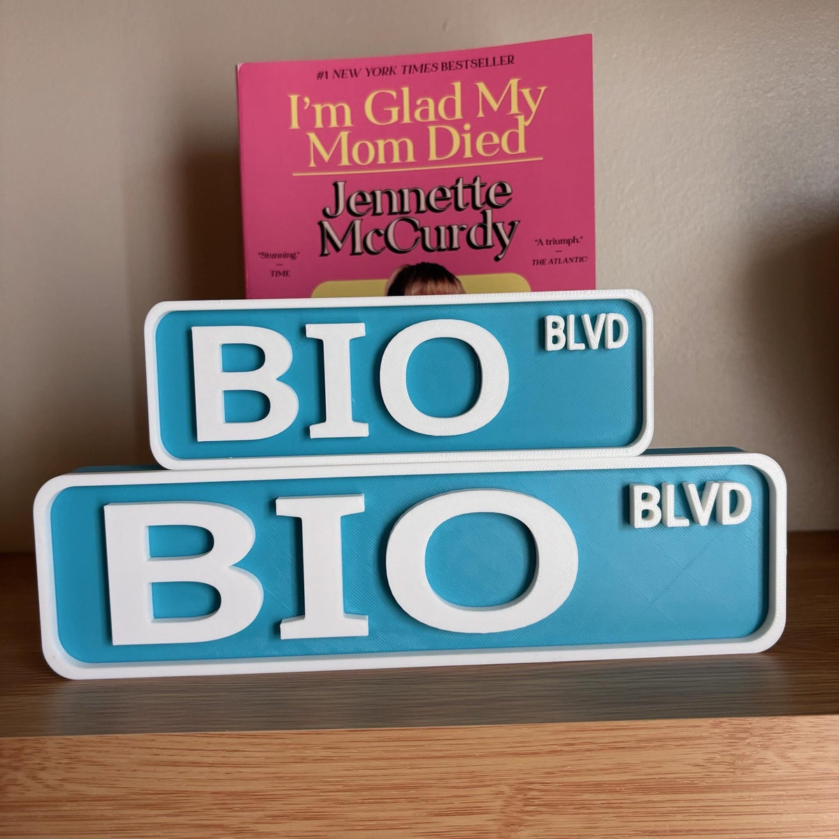 Small and large teal and white BIO BLVD street signs stacked on a wooden shelf
