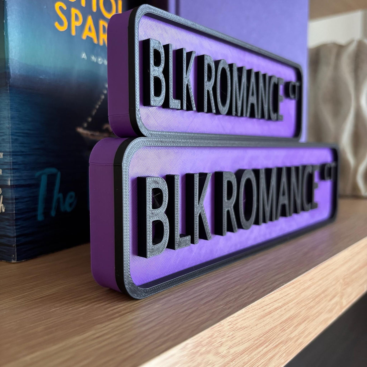 Angled view of the purple BLK ROMANCE CT street signs with raised black lettering