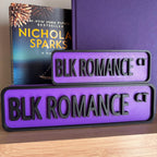 Small and large purple and black BLK ROMANCE CT bookshelf street signs in front of books