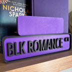 Back of the small purple sign behind the large BLK ROMANCE CT street sign