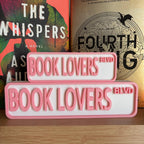 Pink and white BOOK LOVERS BLVD street signs, small stacked on large, in front of books