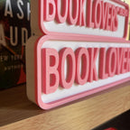 Close angled view of the raised pink lettering on the BOOK LOVERS BLVD street signs