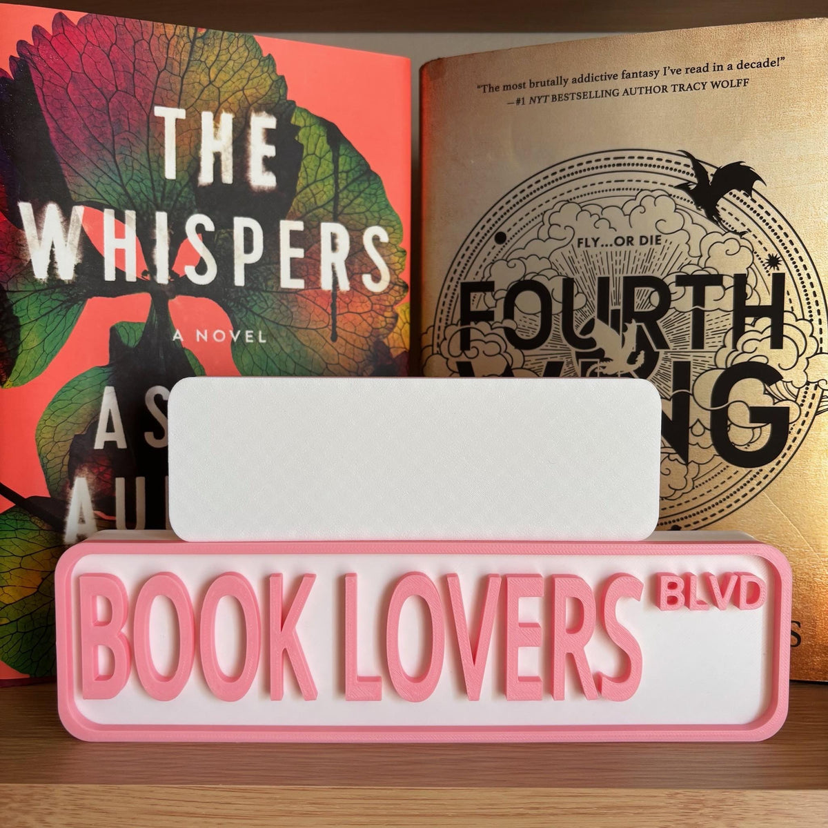 Back of the small white sign behind the large pink and white BOOK LOVERS BLVD street sign