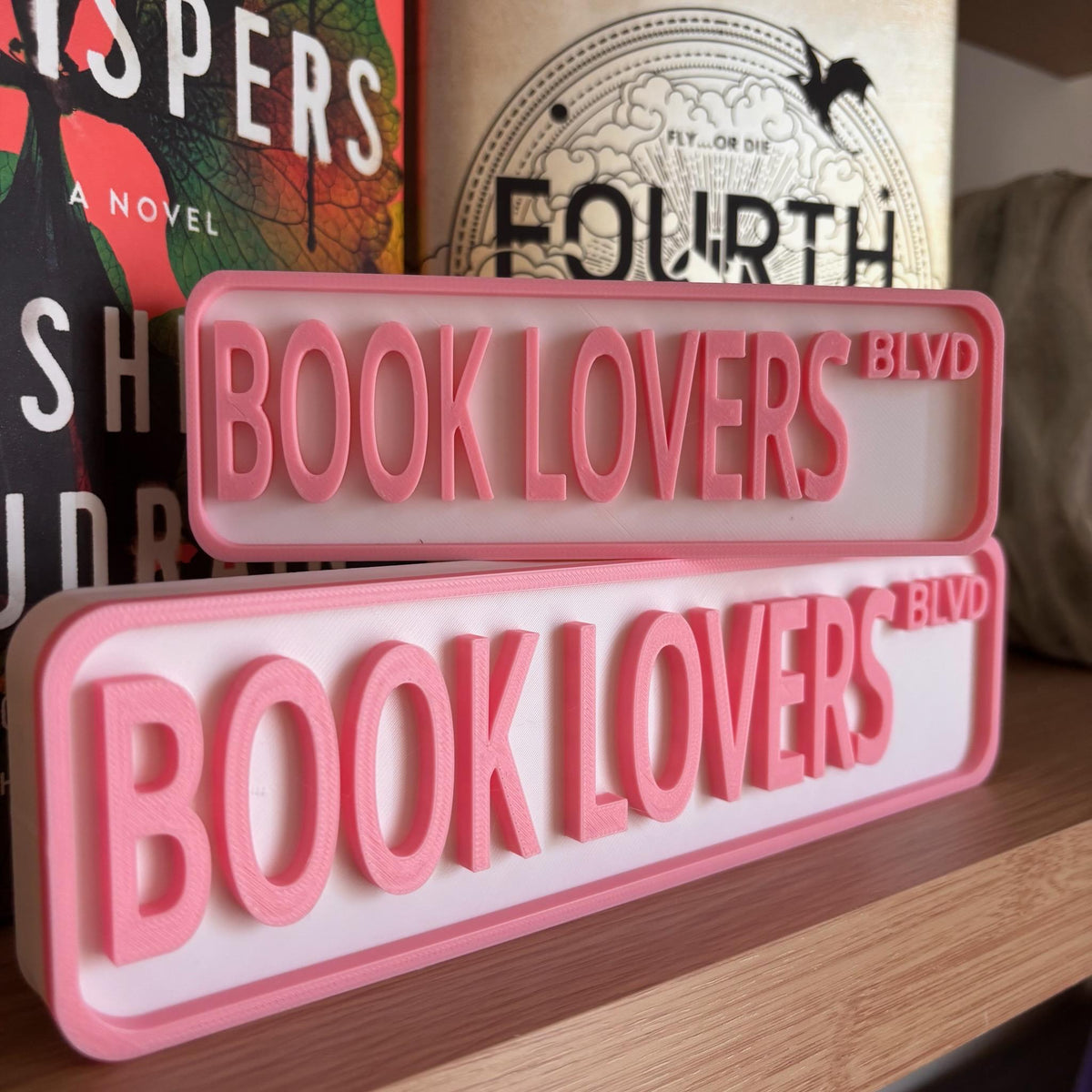 Small and large BOOK LOVERS BLVD street signs in pink and white on a shelf