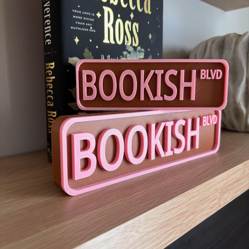 Brown and pink BOOKISH BLVD street signs, small stacked on large, on a bookshelf