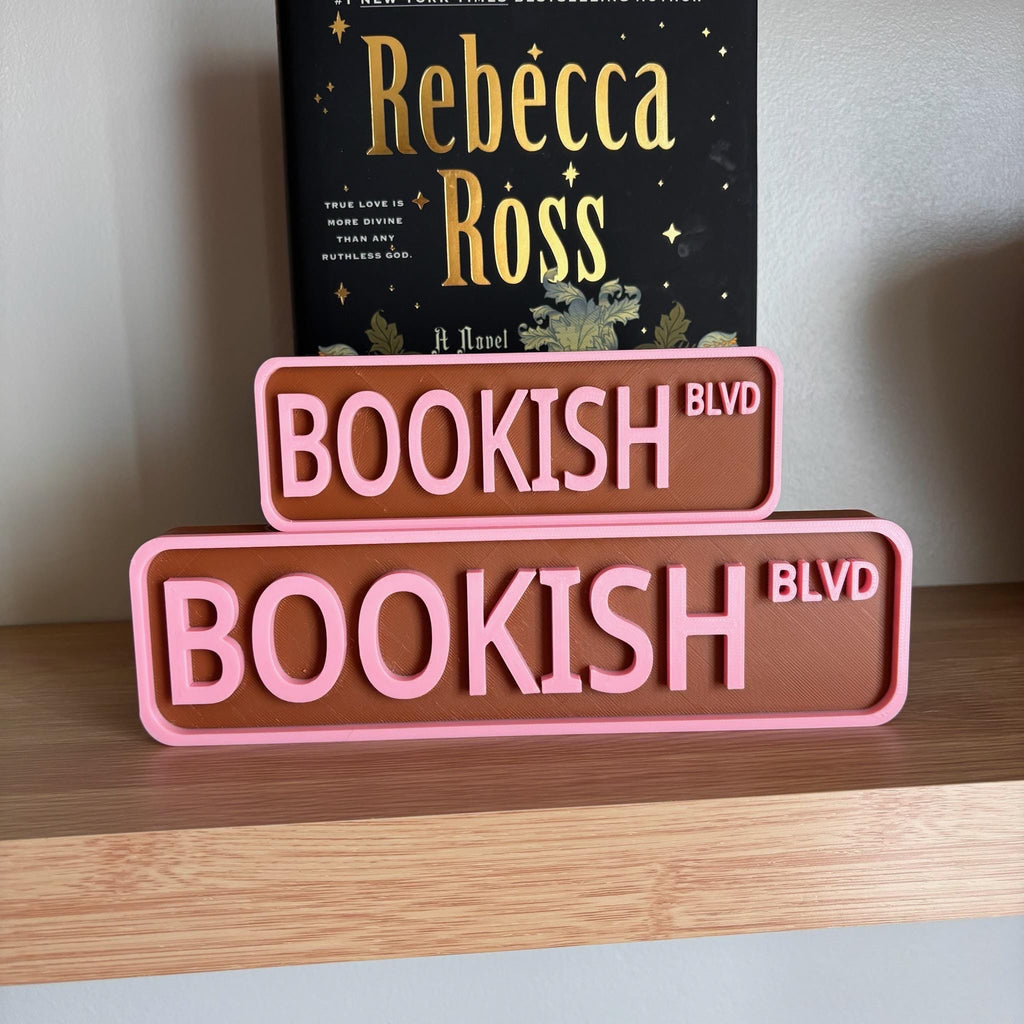 Front view of the small and large brown and pink BOOKISH BLVD street signs