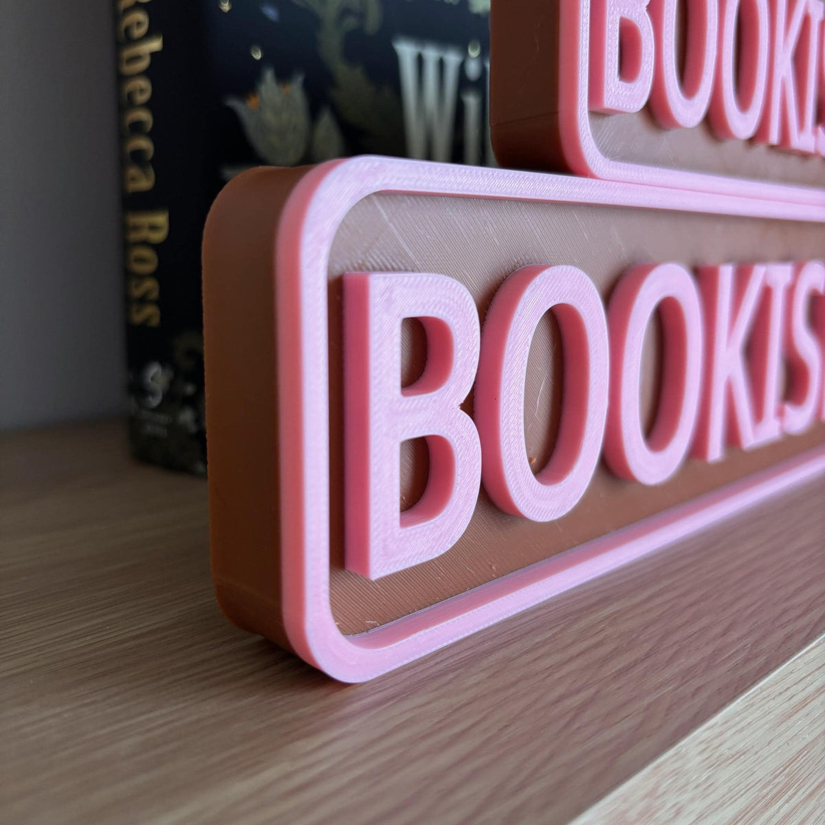Close angled view of the raised pink lettering on the brown BOOKISH BLVD street sign
