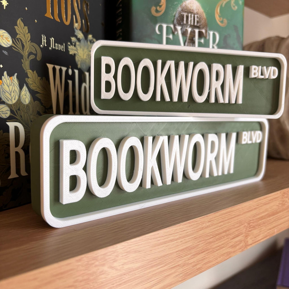 Olive green and white BOOKWORM BLVD street signs, small stacked on large, on a bookshelf
