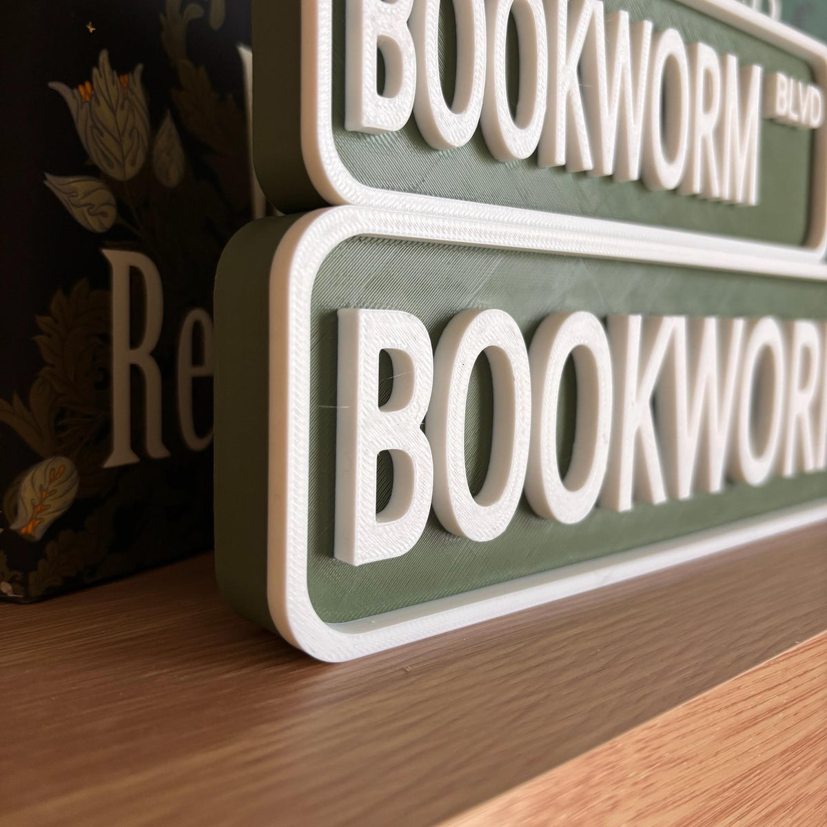 Close angled view of the raised white lettering on the green BOOKWORM BLVD street signs