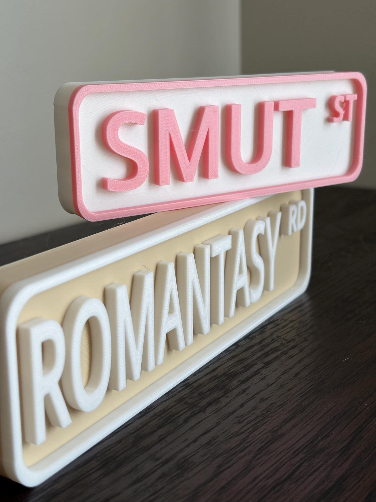 Pink SMUT ST and beige ROMANTASY RD bookshelf street signs
