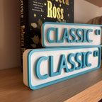 Teal and white CLASSIC CT street signs, small stacked on large, on a bookshelf