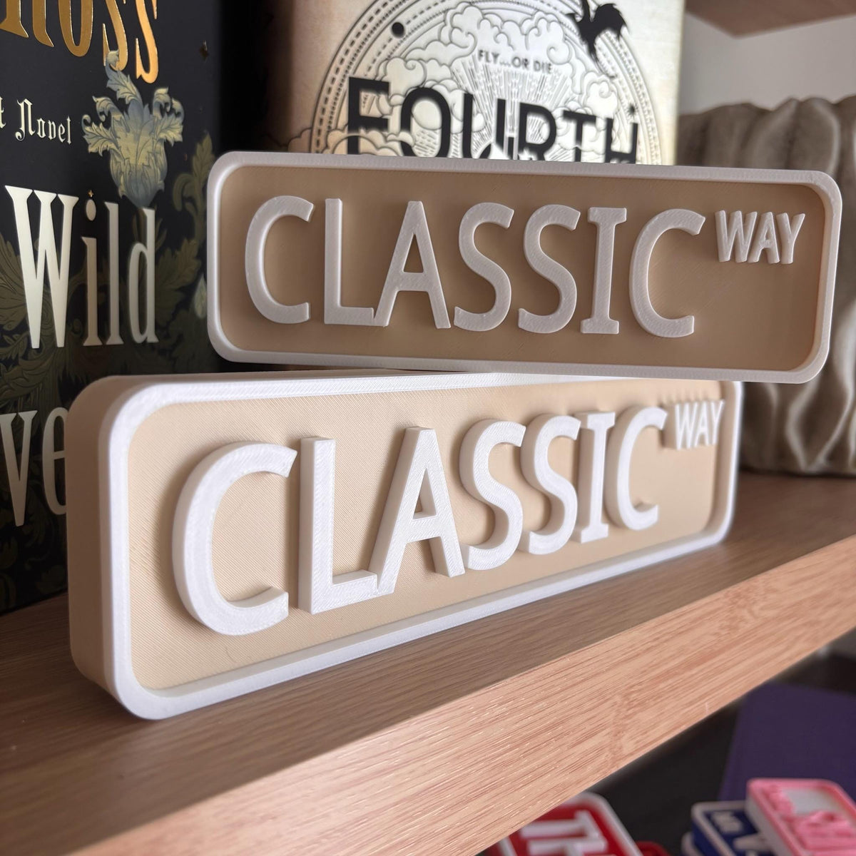 Beige and white CLASSIC WAY street signs, small stacked on large, on a bookshelf