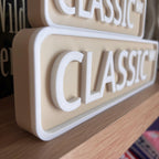 Close angled view of the raised white lettering on the beige CLASSIC WAY street sign