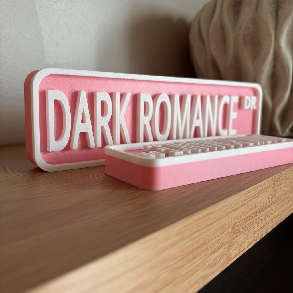 Side profile of the pink and white DARK ROMANCE DR street signs on a shelf