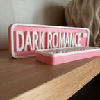 Side profile of the pink and white DARK ROMANCE DR street signs on a shelf