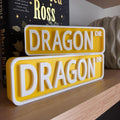 Yellow and white DRAGON DR street signs, small stacked on large, on a bookshelf
