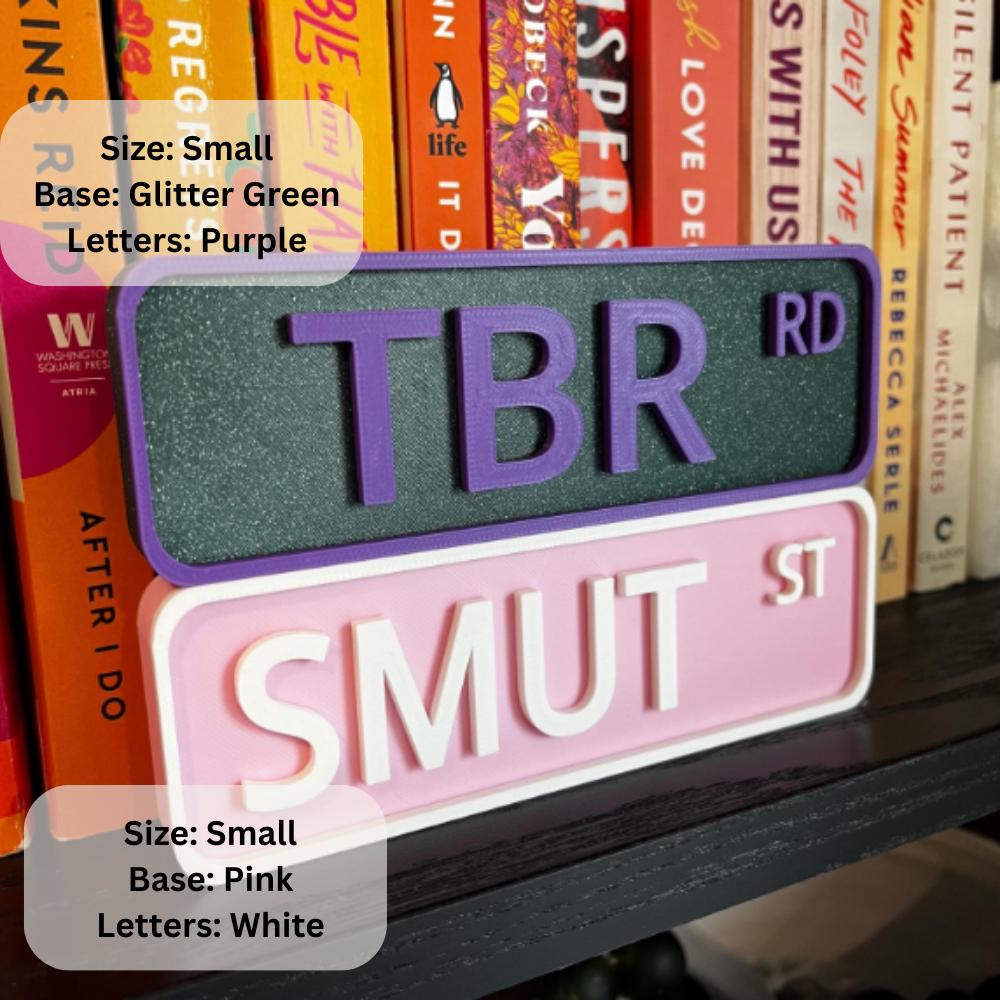 Small TBR RD sign in glitter green with purple letters and SMUT ST sign in pink with white letters