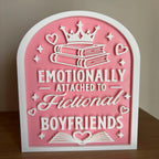 Emotionally Attached to Fictional Boyfriends bookshelf sign, a pink and white arched 3D printed sign with a crown, stacked books and hearts, standing on a wooden shelf