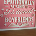 Close-up of the raised white lettering Attached to Fictional Boyfriends with hearts, sparkles and an open book on the pink sign