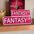 Magenta and white FANTASY CIR street signs, small stacked on large, in front of a book