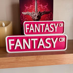 Magenta and white FANTASY CIR street signs, small stacked on large, in front of a book