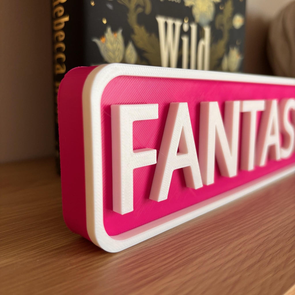 Close angled view of the raised white lettering on the magenta FANTASY CIR street sign