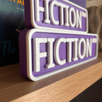 Close angled view of the raised white lettering on the purple FICTION BLVD street signs