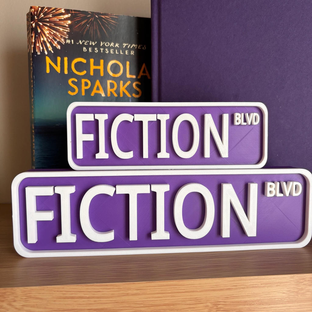 Front view of the small and large purple and white FICTION BLVD street signs