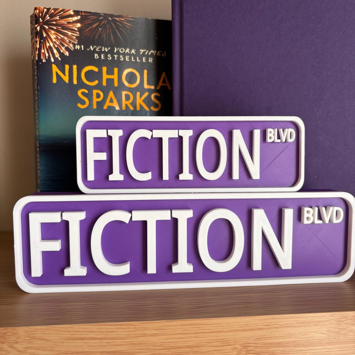 Front view of the small and large purple and white FICTION BLVD street signs
