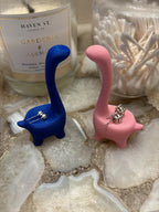 Two dinosaur shaped earring holders, one blue and one pink, with silver earrings on each holder. __etsy:6791612960