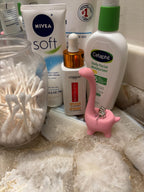 A pink dinosaur figurine with two silver earrings on its back. The figurine is on a white and gray surface in a bathroom. __etsy:6839619453