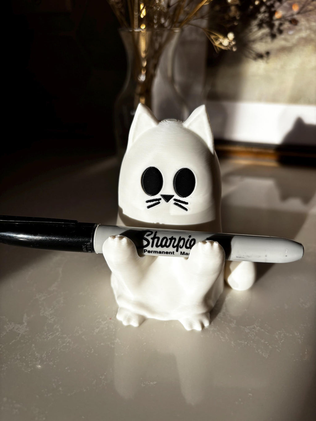 A white cat-shaped ghost with black eyes and whiskers is holding a black Sharpie permanent marker on a glossy surface, with a blurred background. __etsy:7207233165
